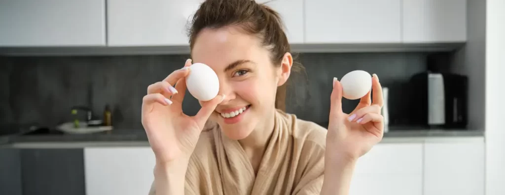 Smiling woman holding two eggs in kitchen