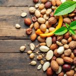 Assorted nuts with green leaves on wooden table.